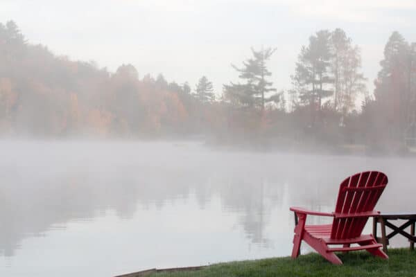 A red Adirondack chair along the shores of Flower Lake in Saranac Lake, NY