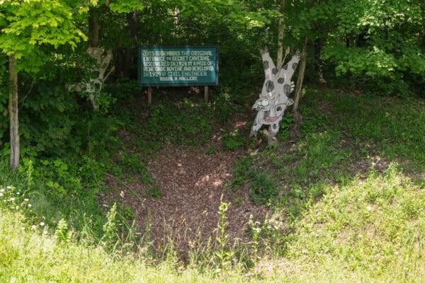 A wooden cow and sign sit next to the original entrance to Secret Caverns in Howes Cave, NY